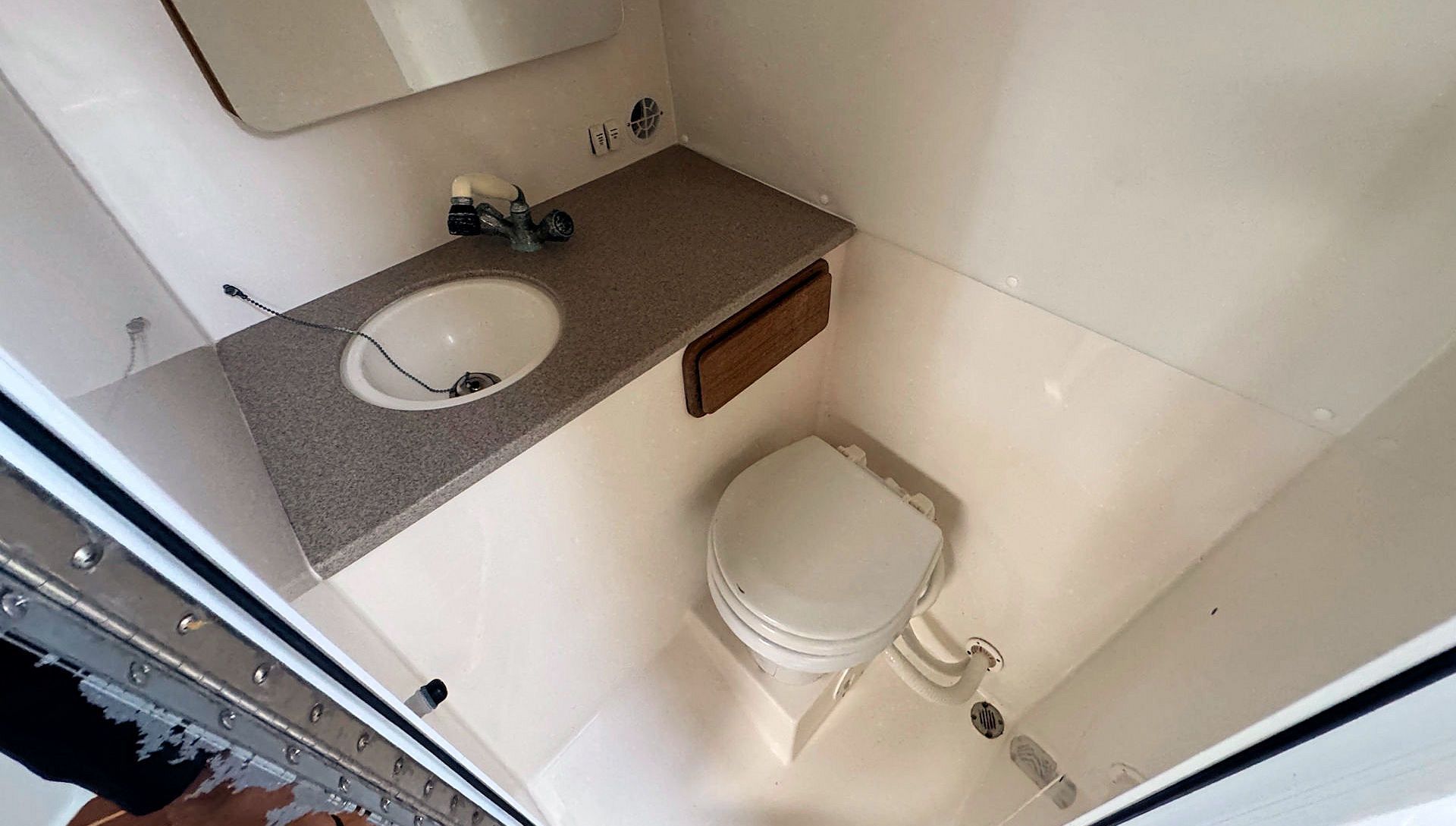 Compact bathroom with sink, toilet, and small countertop in a narrow, white-walled space