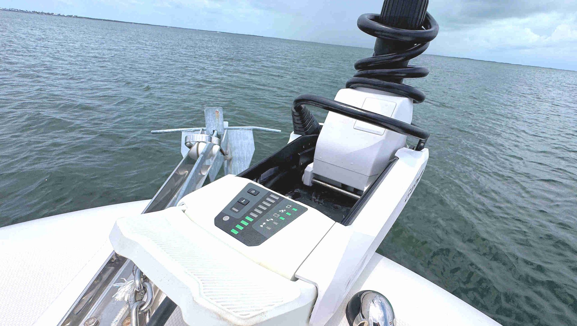 Trolling motor and controls on a white motorboat with open water in the background