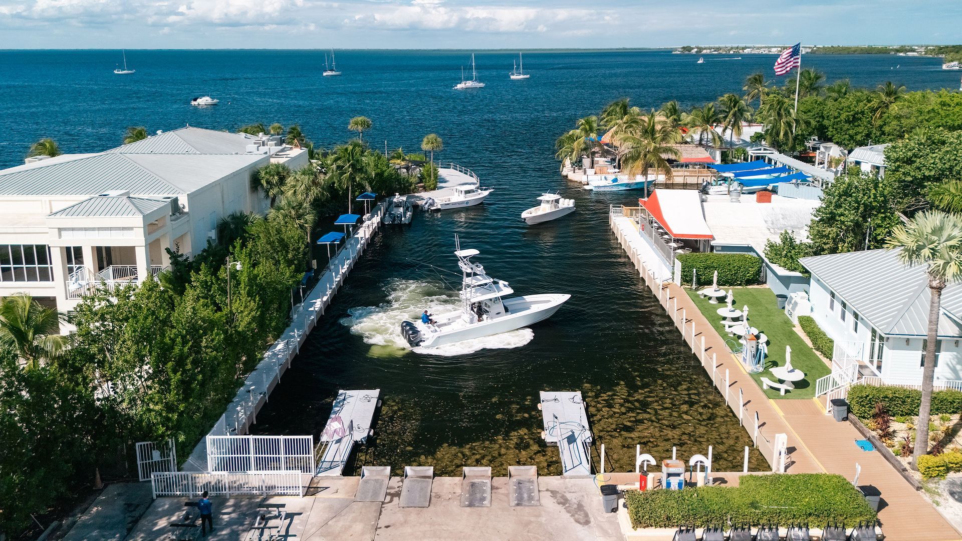 Boat channel with yachts between waterfront buildings, leading to a blue ocean on a sunny day