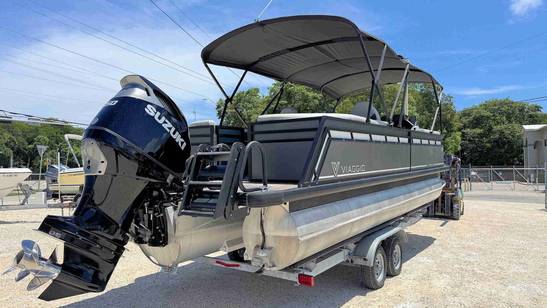 Tritoon boat with black bimini top and outboard motor on a trailer in a gravel lot