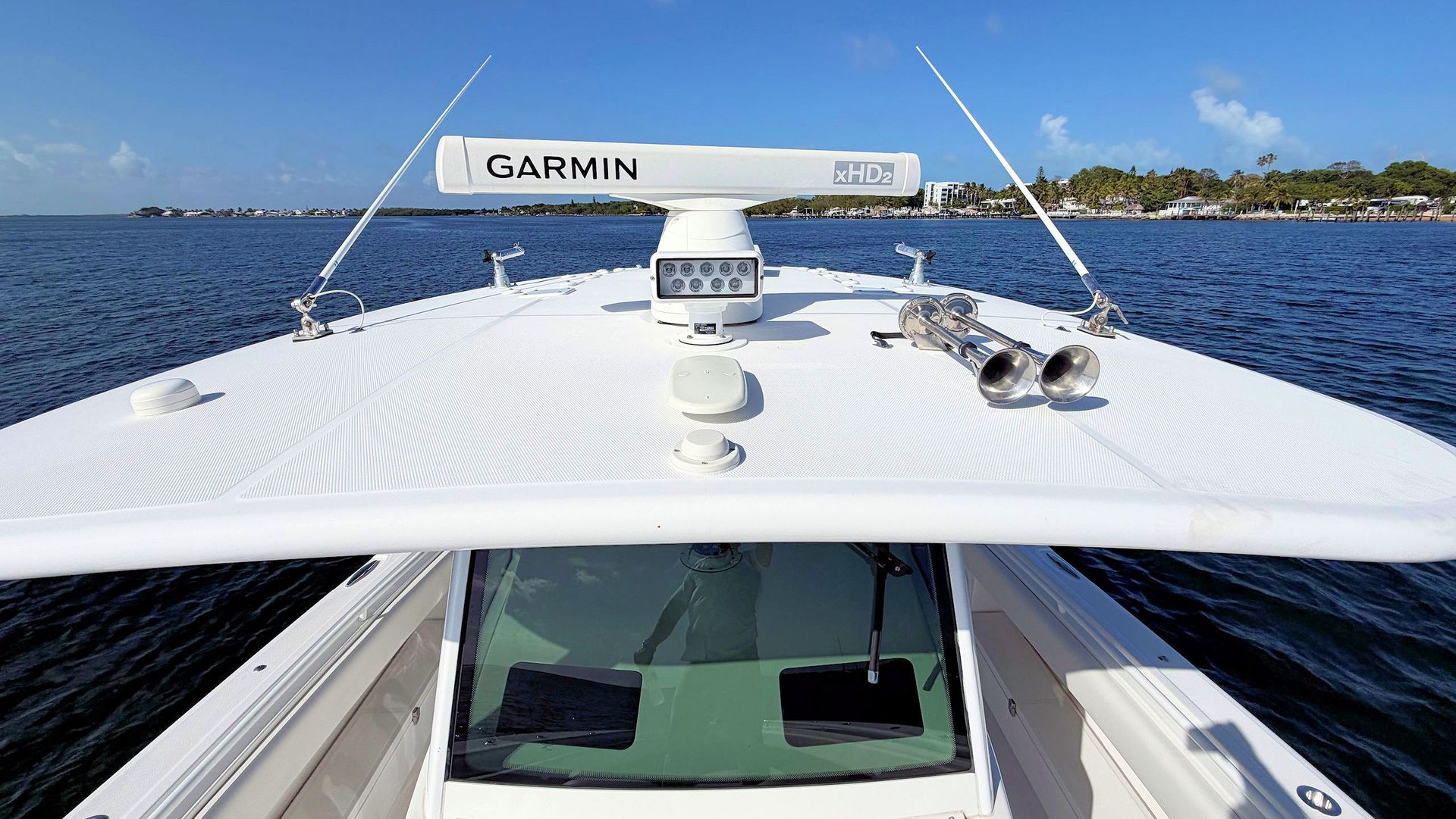 View of top of hard-top with Garmin radar and white patterned deck, seen over open water with a shoreline in the distance
