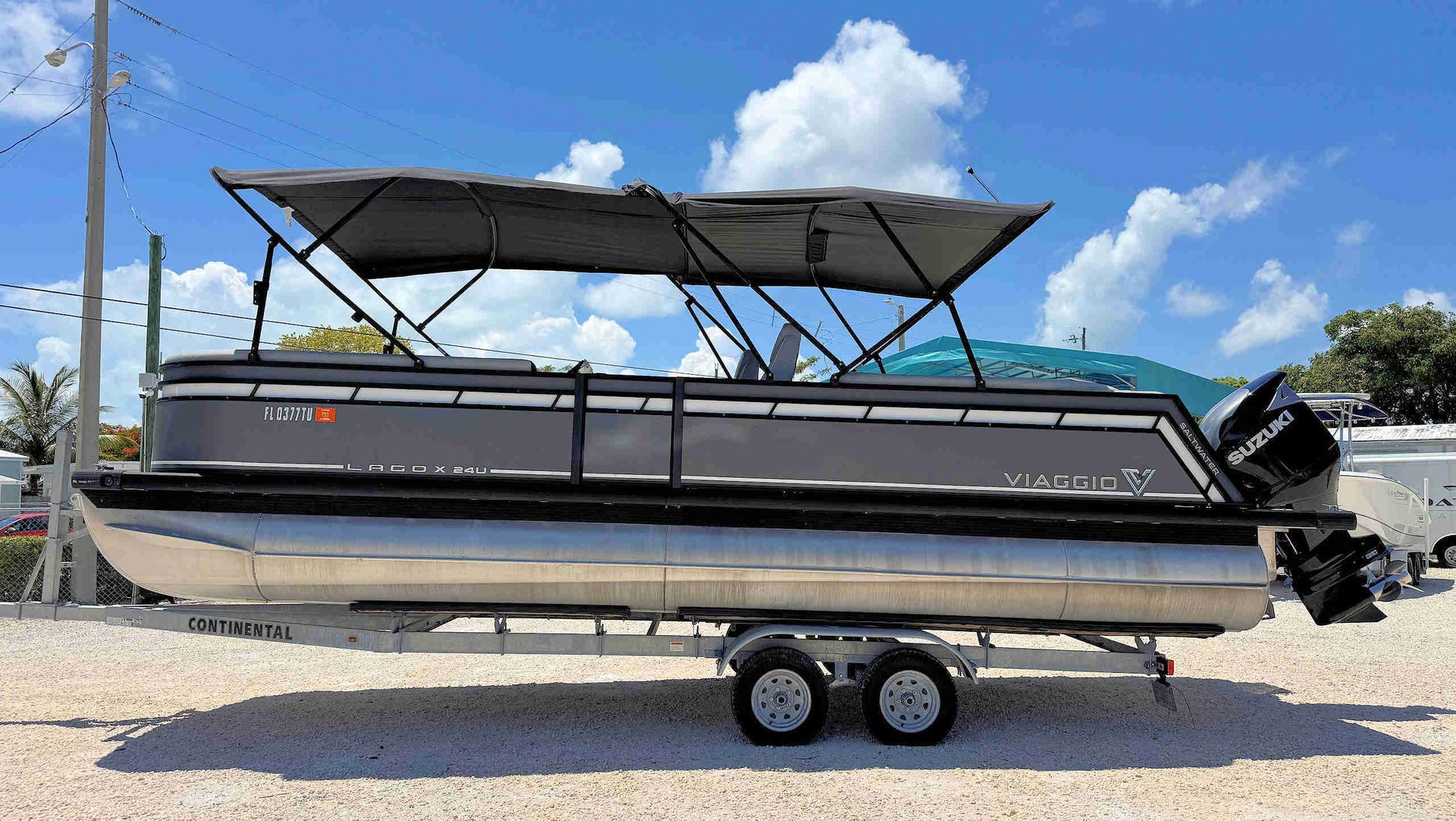 Black Tritoon boat on a trailer with a black bimini top, parked outdoors on gravel.