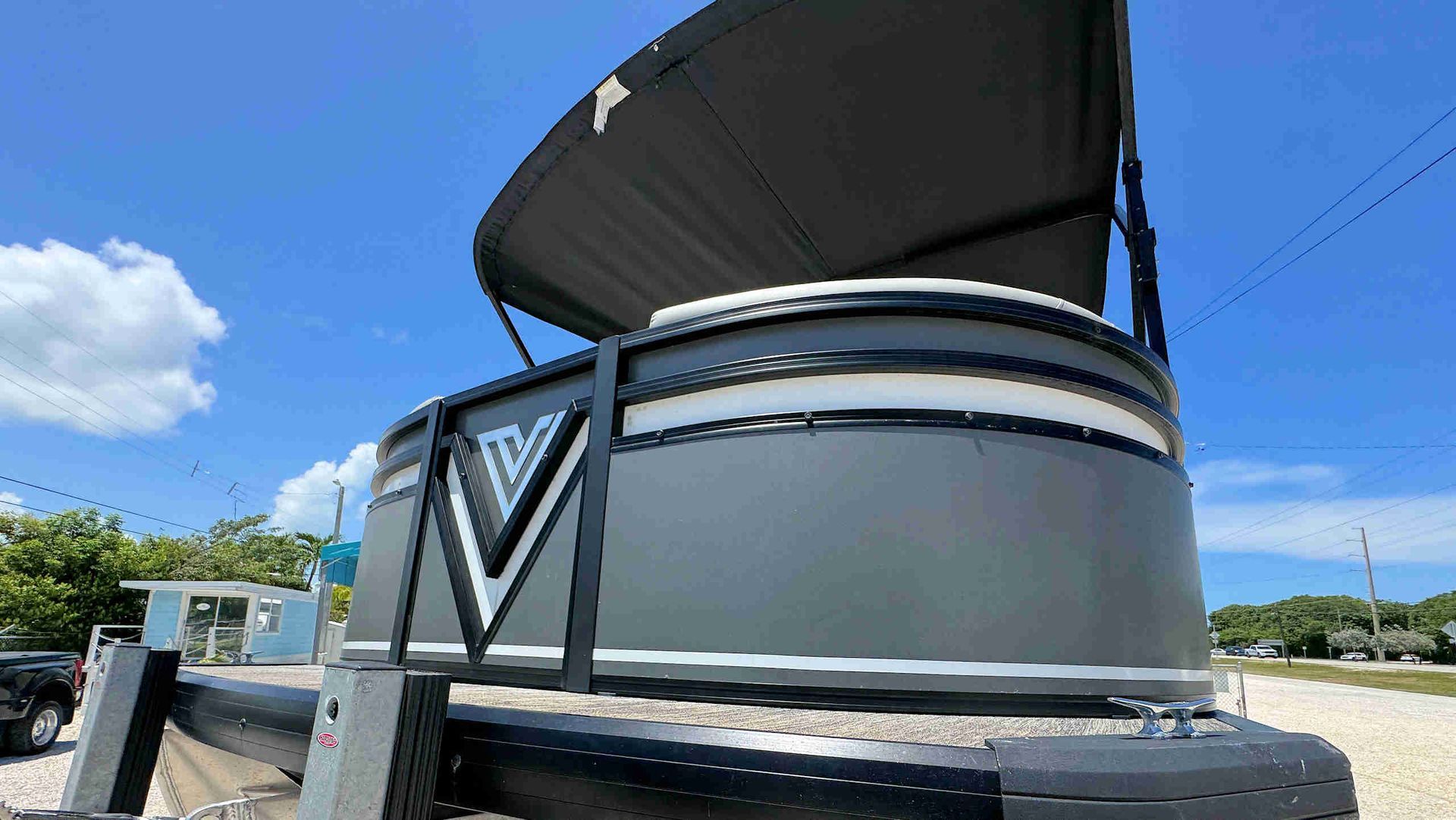 Black Tritoon boat with a raised canopy on a sunny day, seen from the side at a dock.