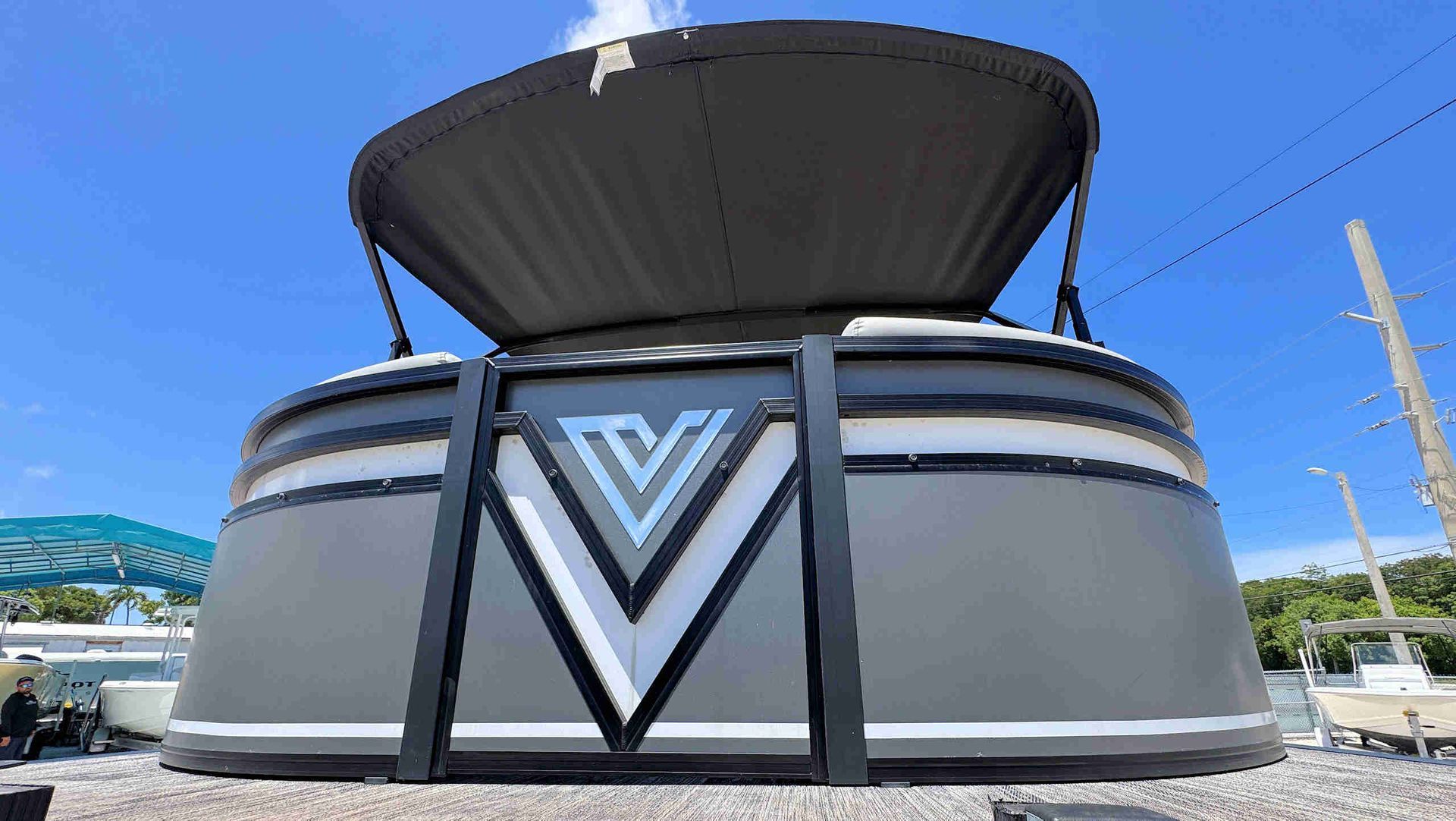 Large gray structure with a black V-shaped emblem and an open black  bimini top against a blue sky.