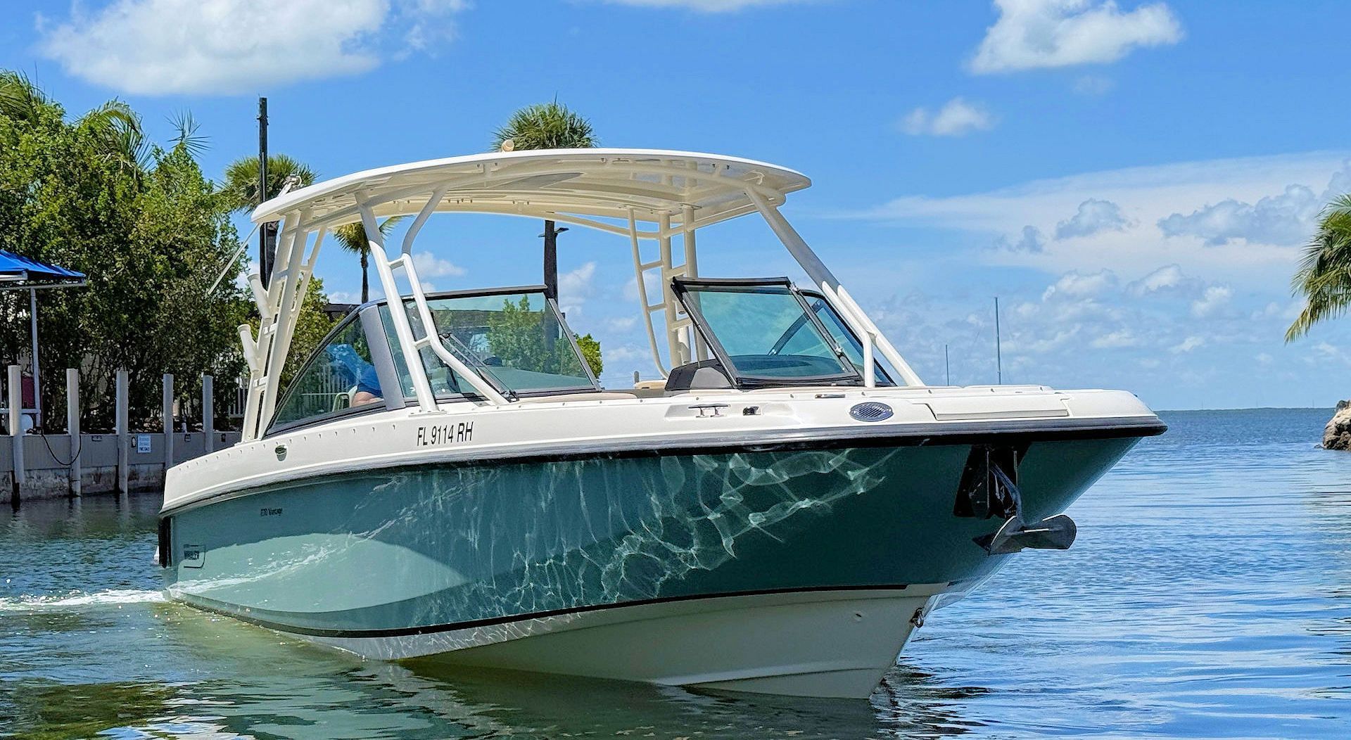 A teal and white dual-console motorboat with a hardtop roof drifting in calm, sunny coastal waters.