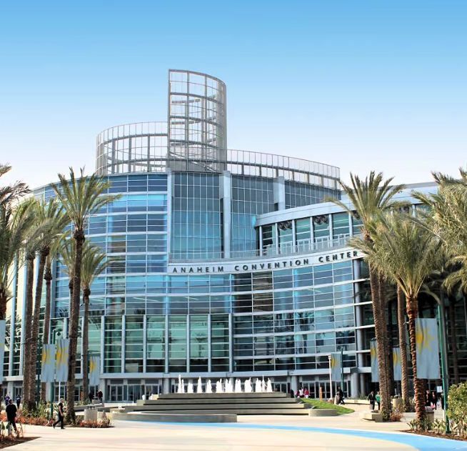 Anaheim Convention Center Anaheim Convention Center building exterior, glass facade, palm trees, blue sky.