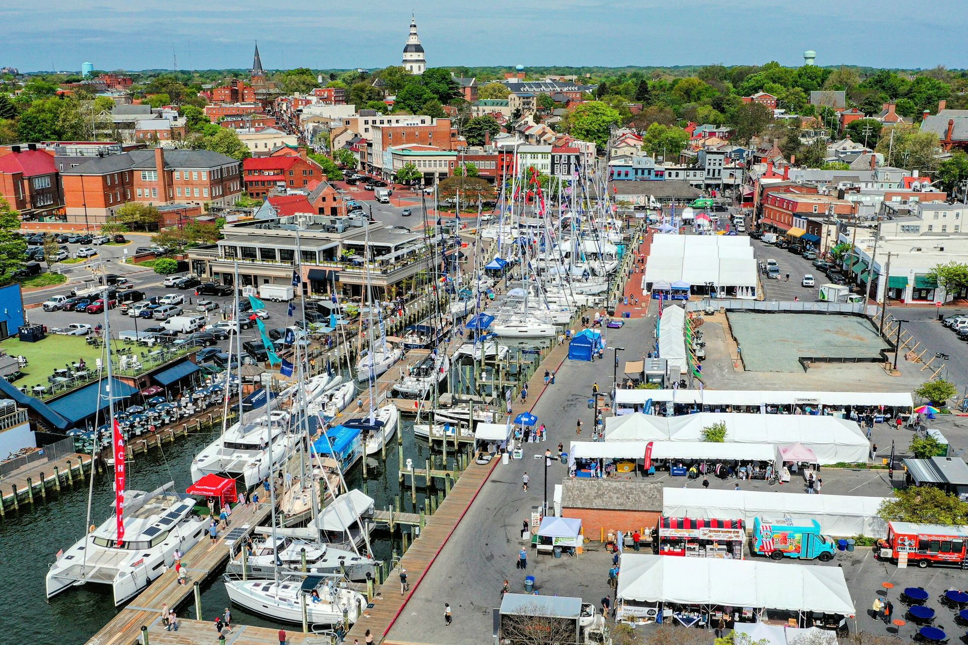 Annapolis Spring Sailboat Show Aerial view of Annapolis harbor with sailboats, docks, buildings, and a festival with tents.
