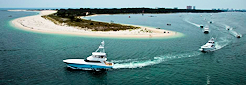 Boats travel through teal-colored water near a sandy beach.