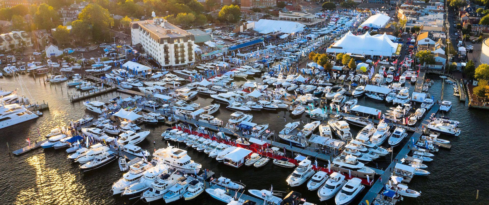 Annapolis Powerboat Show Aerial view of a boat show with numerous white boats docked in a harbor, and tents on the waterfront.