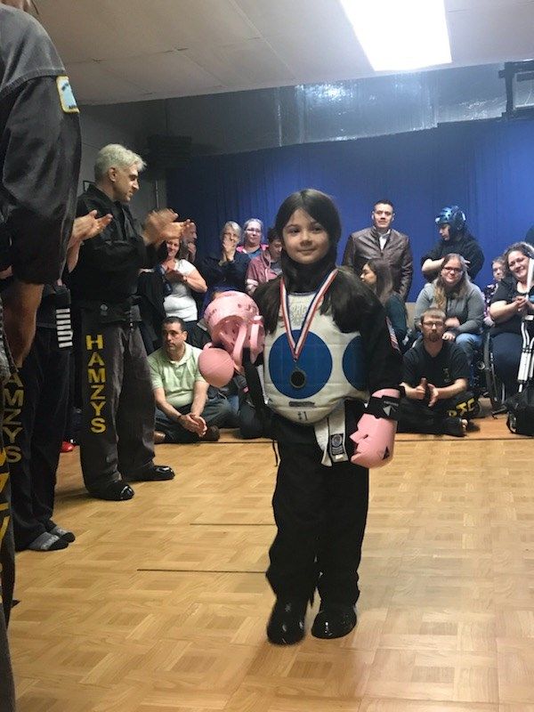 A young girl wearing boxing gloves and a medal stands in front of a crowd