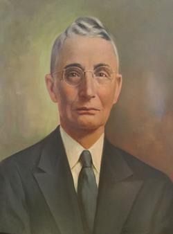 Portrait of a man in a dark suit and tie, wearing glasses, and with neatly combed gray hair.