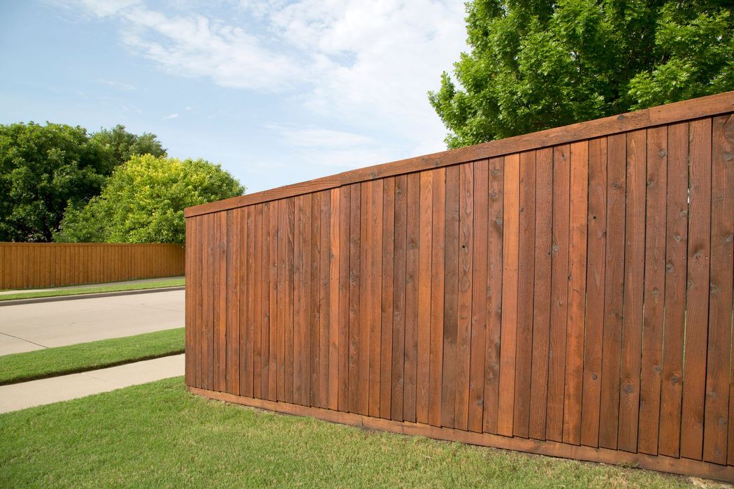 Wooden privacy fence with brown stain, separating a grassy lawn from a street.