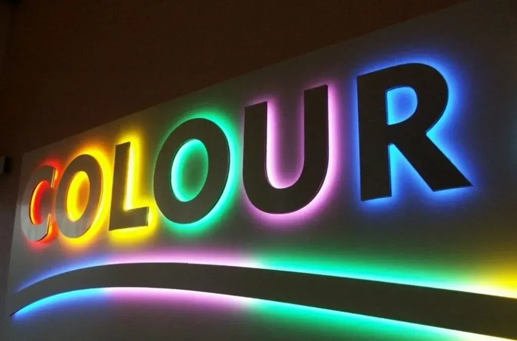 Letrero “Color” con retroiluminación en los colores del arco iris, montado en una pared.