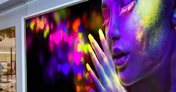 Mujer con pintura facial de neón, levantando la mano, contra un fondo bokeh colorido.