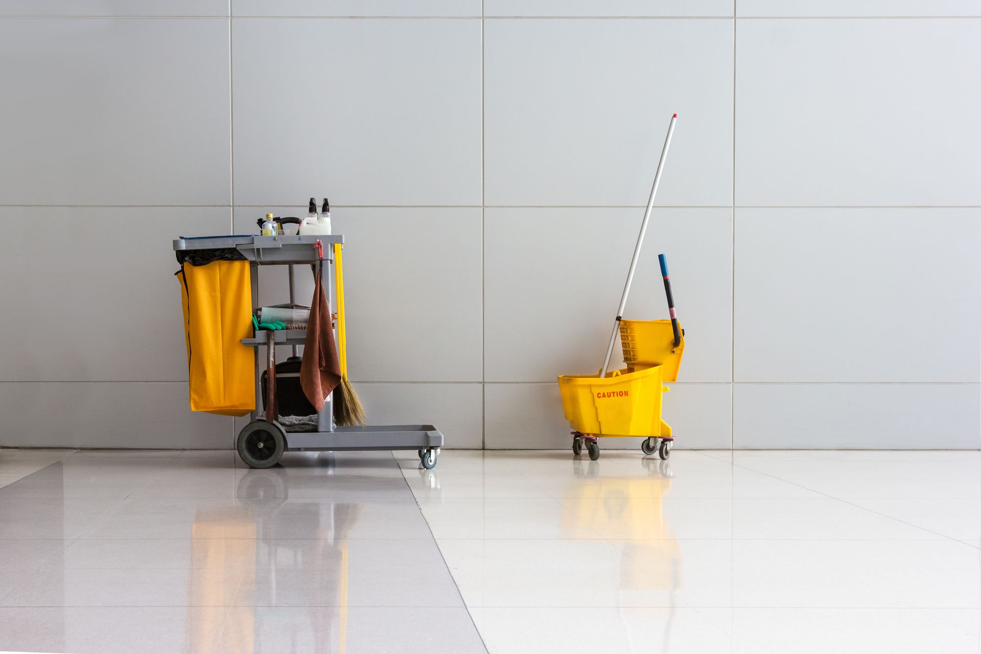 A cleaning cart with a mop and bucket next to a mop bucket.