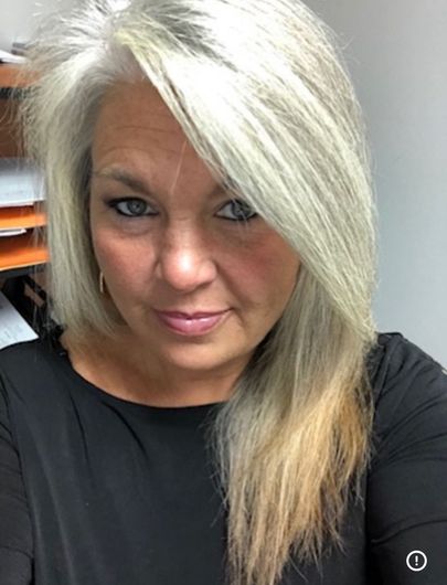 Woman with long, gray and blonde hair, wearing a black shirt, looking at the camera.