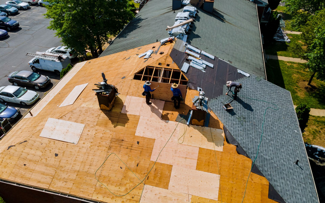 Roofers working on a residential rooftop replacement on a sunny day, seen from above.