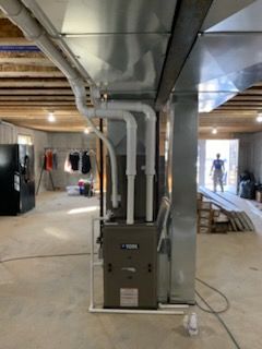 Furnace with connected white pipes in a room under construction.