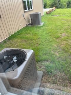 Two brown air conditioning units on concrete pads near a building with a window and grassy area.