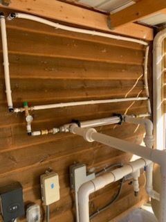 White PVC pipes and electrical boxes on a wooden wall; part of a pool's water system.