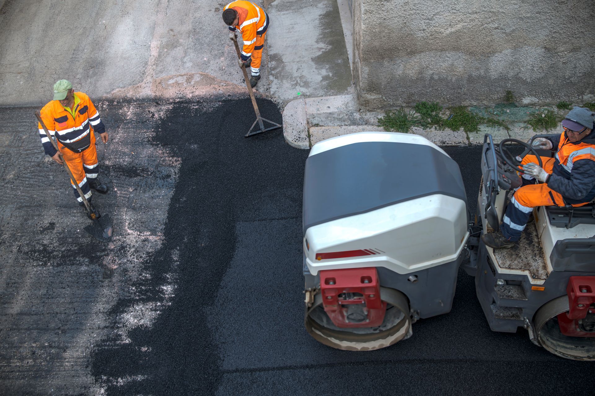 Commercial asphalt contractors in safety vests, are laying fresh asphalt on a street.