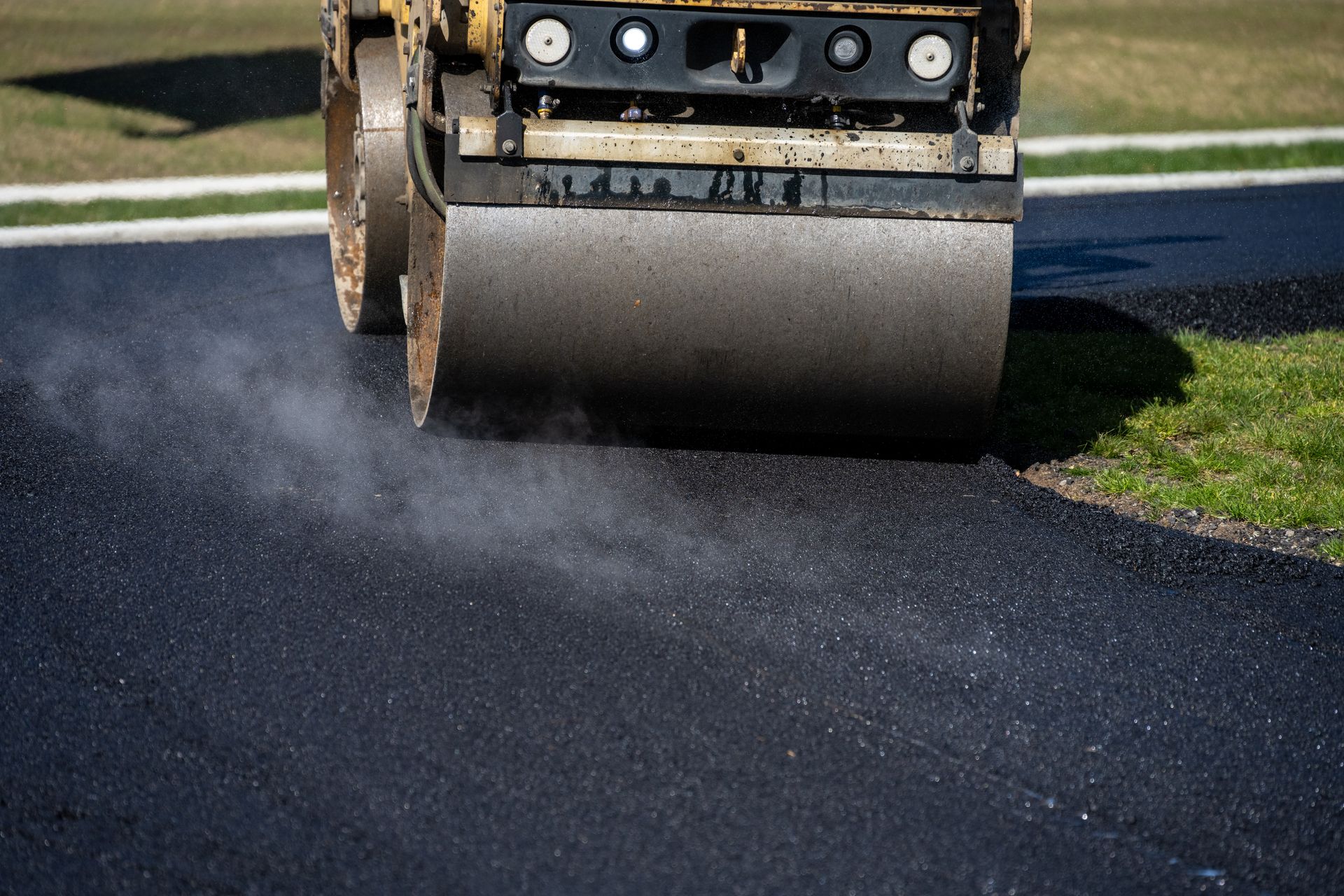 A close-up of a steamroller turning into a freshly paved driveway to compact the hot asphalt.