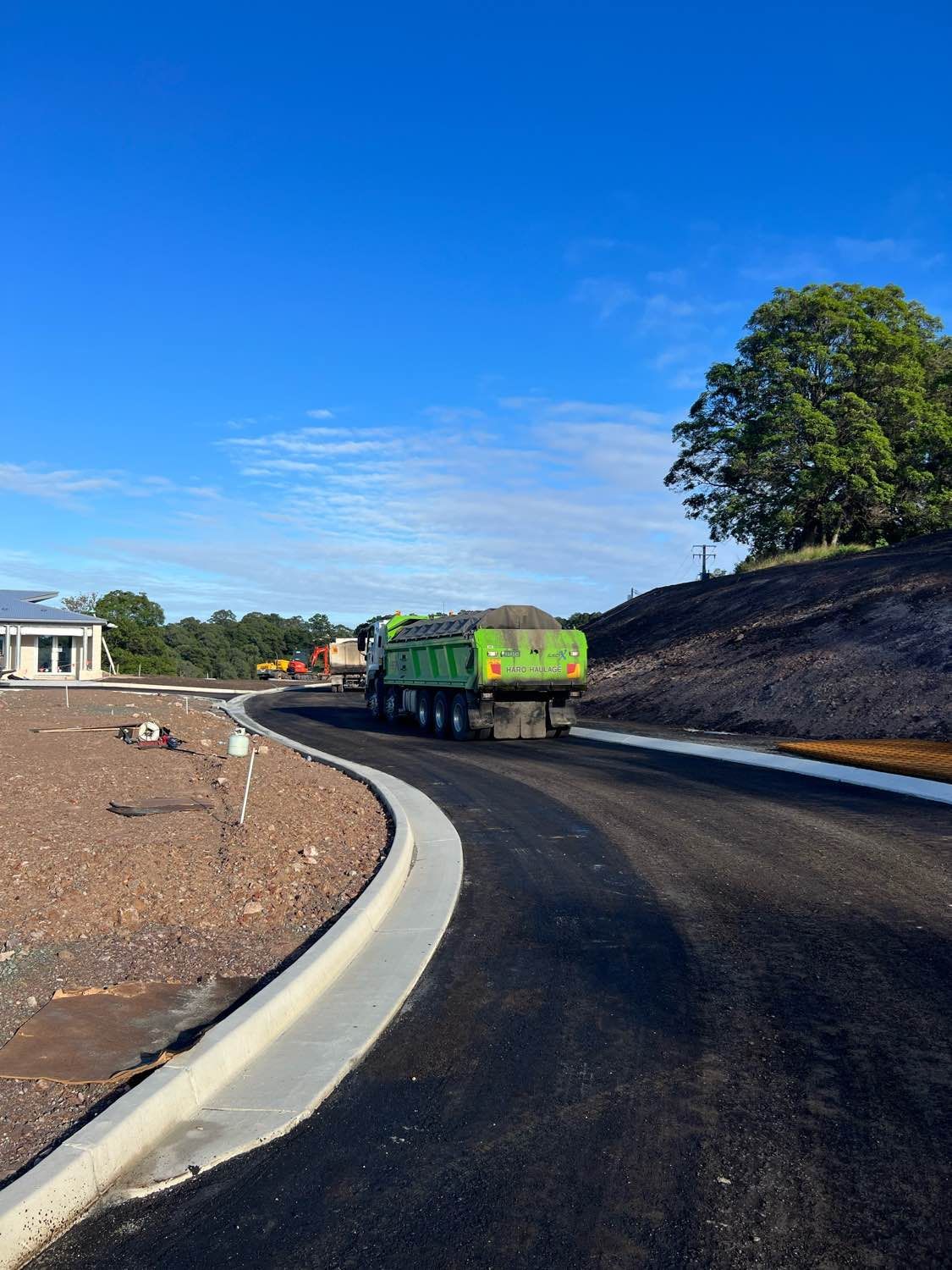 A green dump truck is driving down a curvy road.