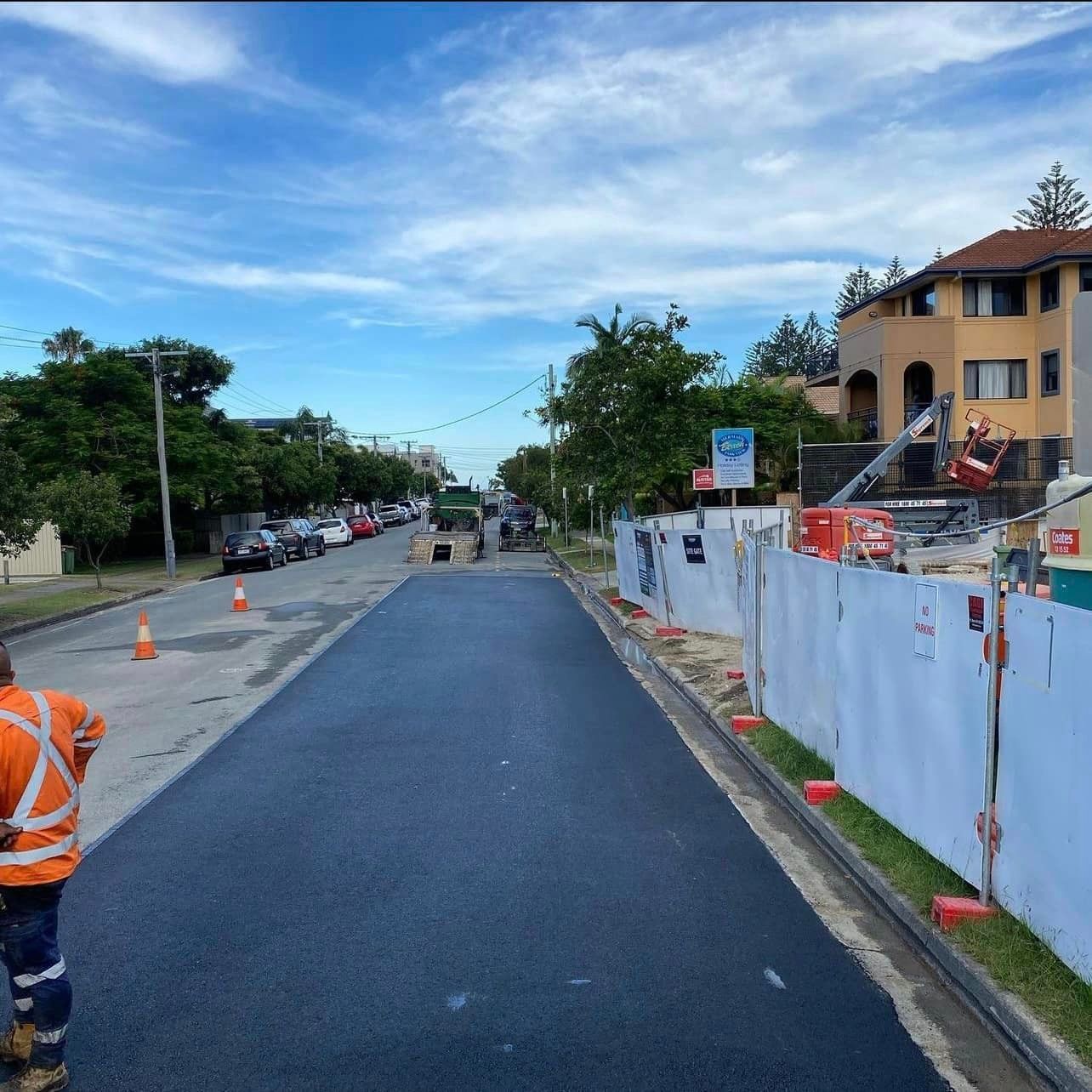 A man in an orange vest is walking down a street