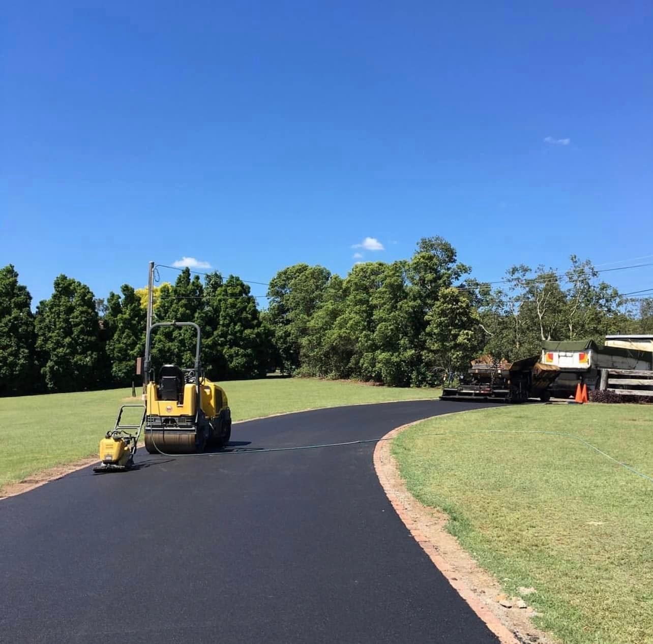 A yellow truck is driving down a road next to a grassy field.