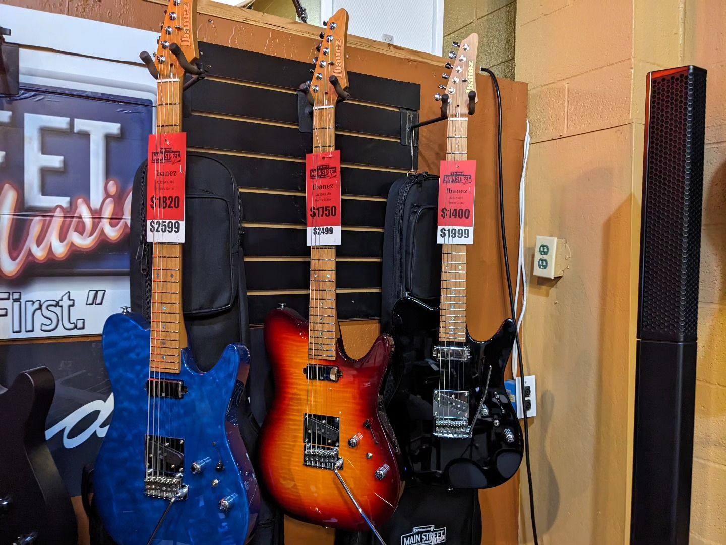 three electric guitars are hanging on a wall in front of a sign that says first