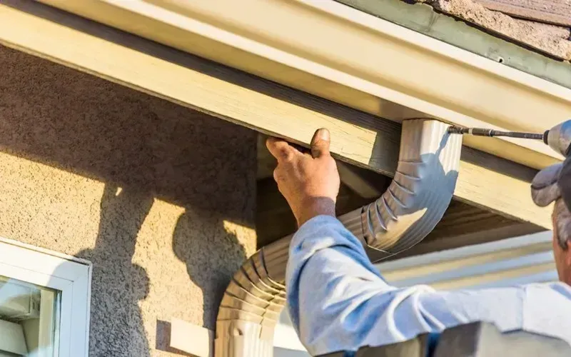 Handyman securing a corrugated aluminum downspout to a home