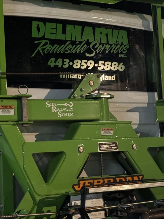 Green Jerr-Dan tow equipment in front of Delmarva Roadside Services sign with phone number
