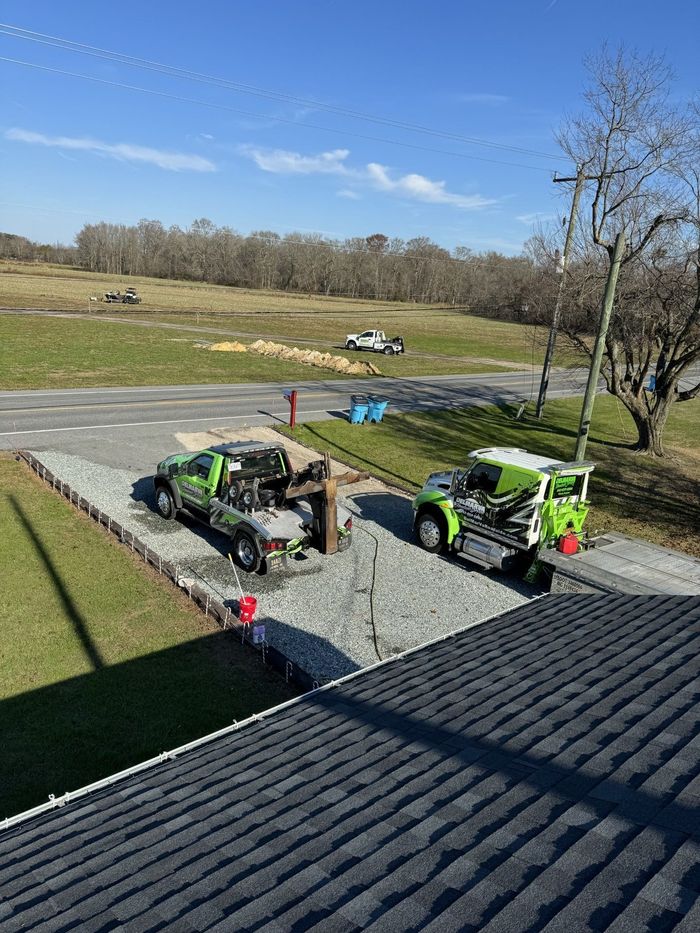 Two green utility vehicles parked on gravel beside a field under a clear blue sky
