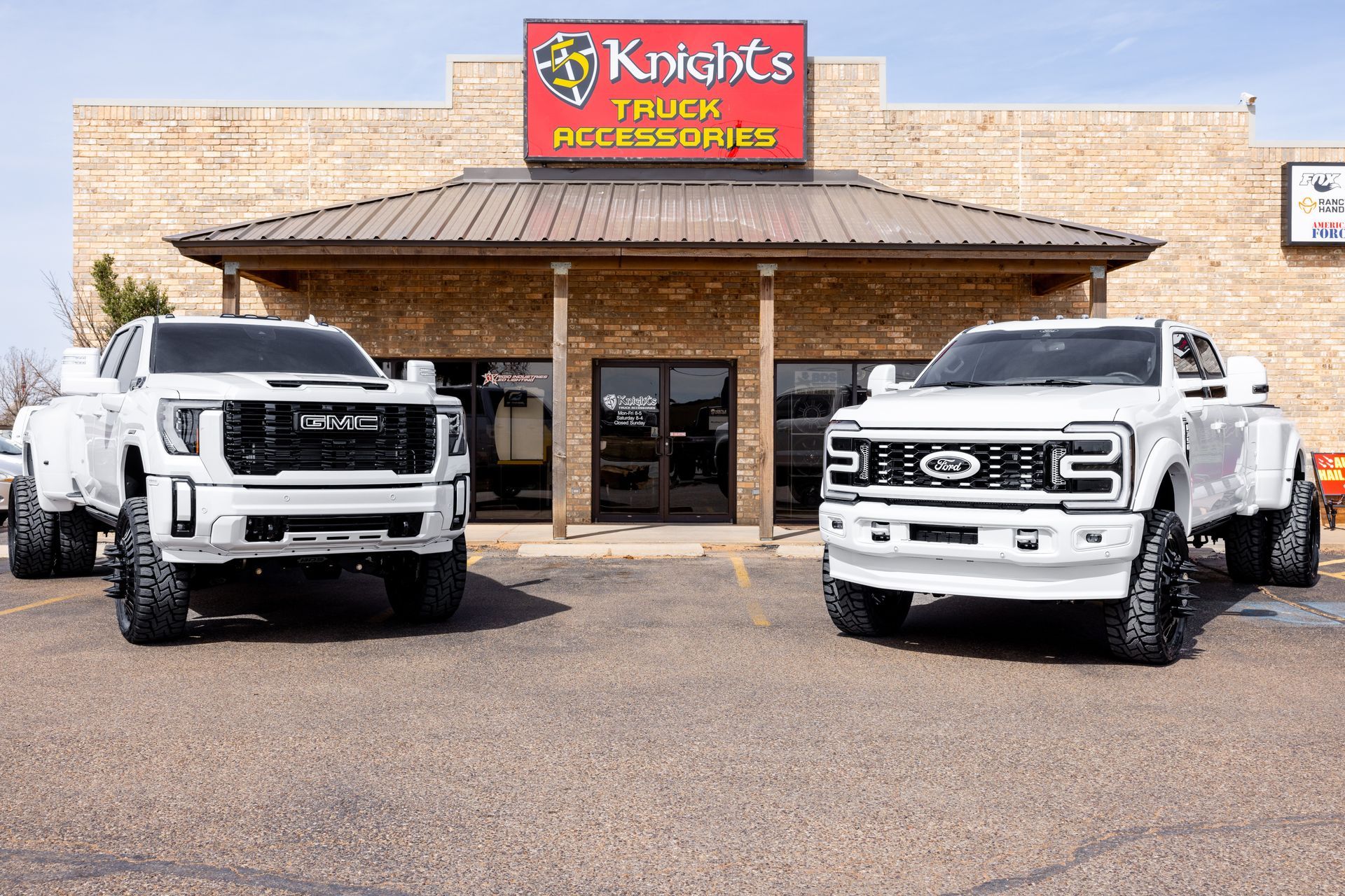 Two white trucks are parked in front of a truck accessories store.