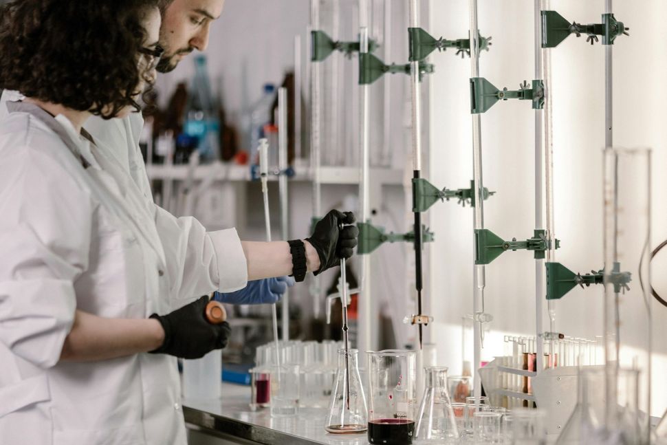 Scientist in a lab coat using pipettes and glassware at a laboratory workstation