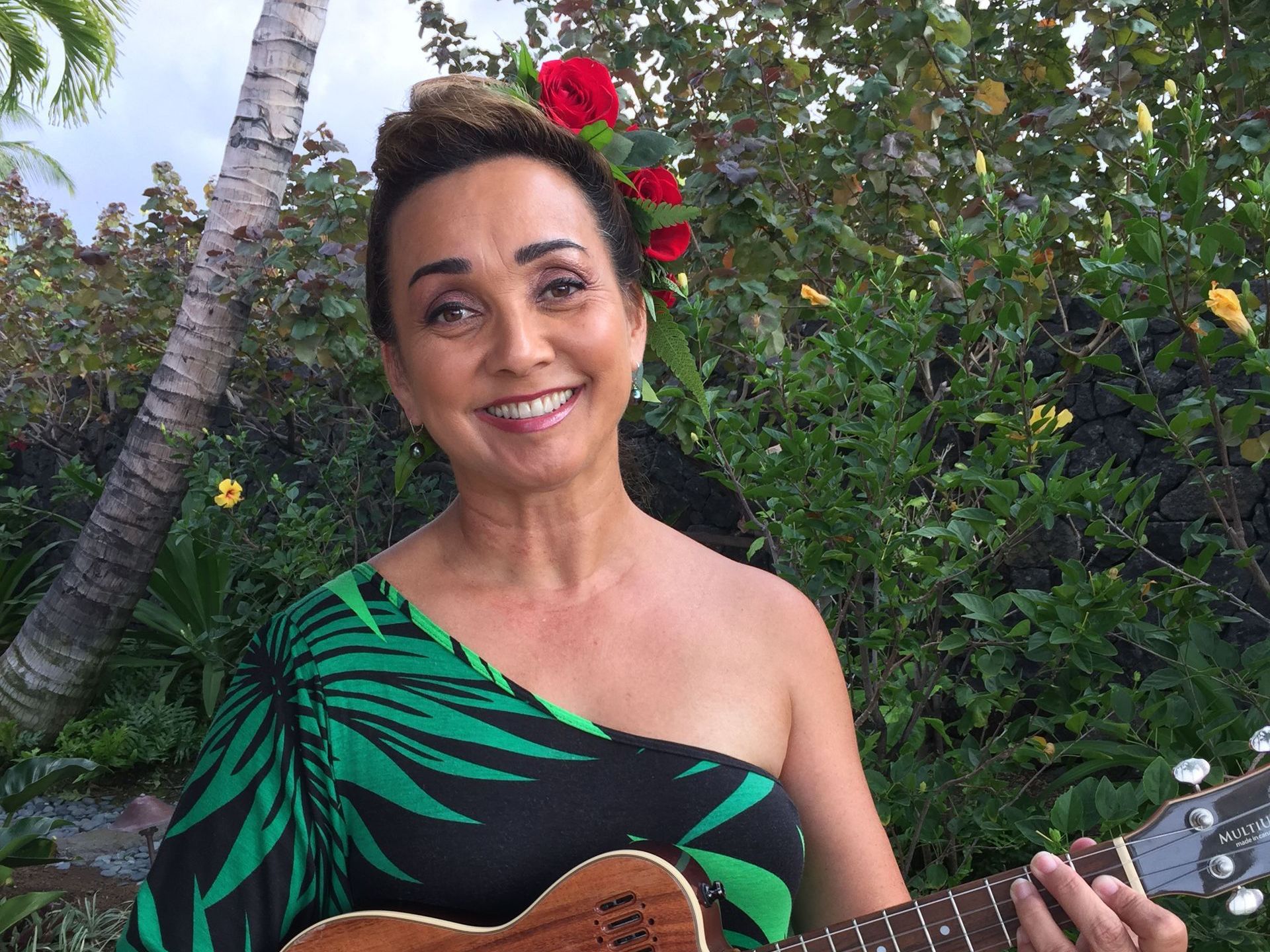 A woman in a green dress is holding a guitar and smiling.