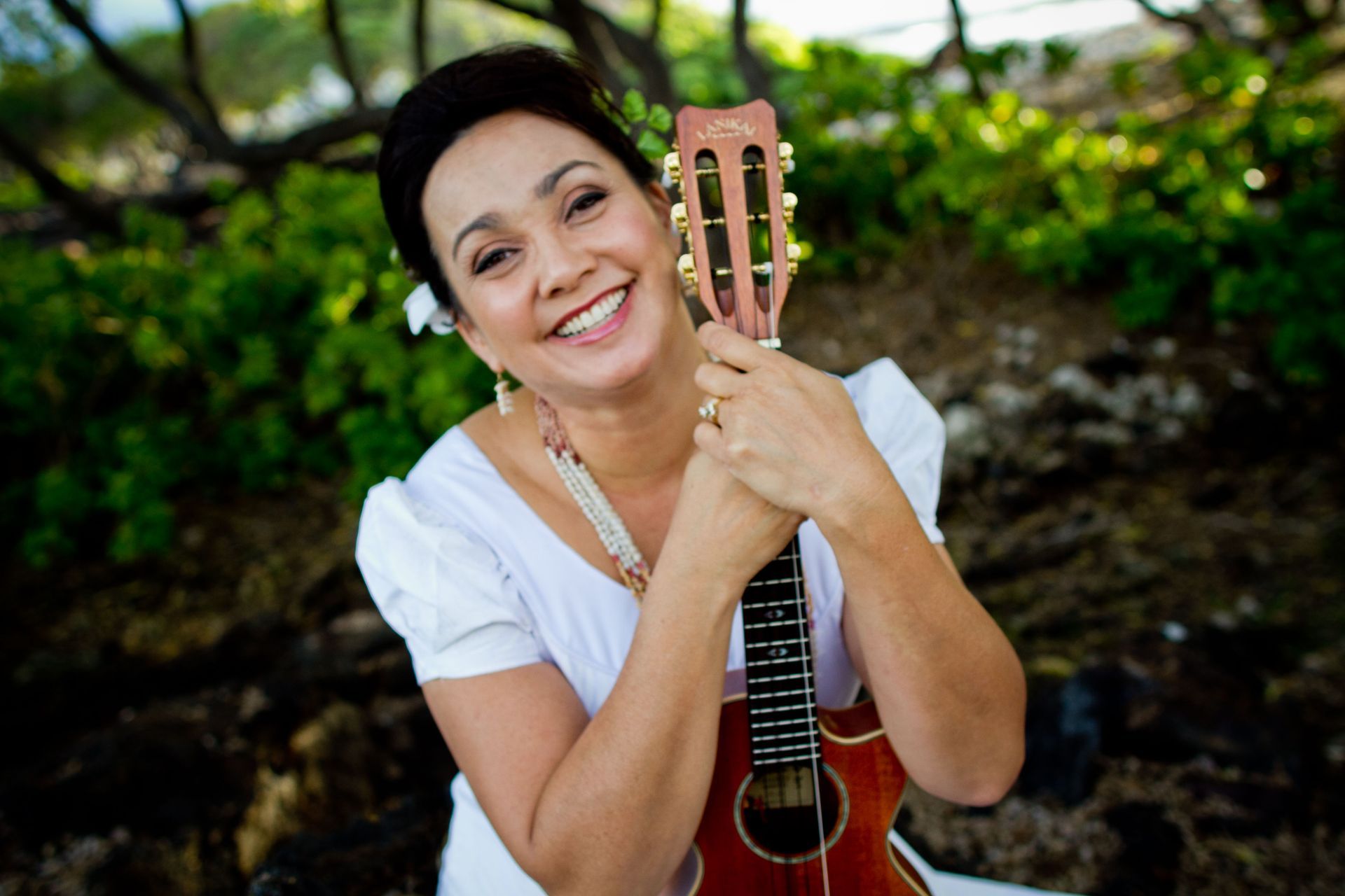 A woman in a white dress is holding a guitar and smiling.