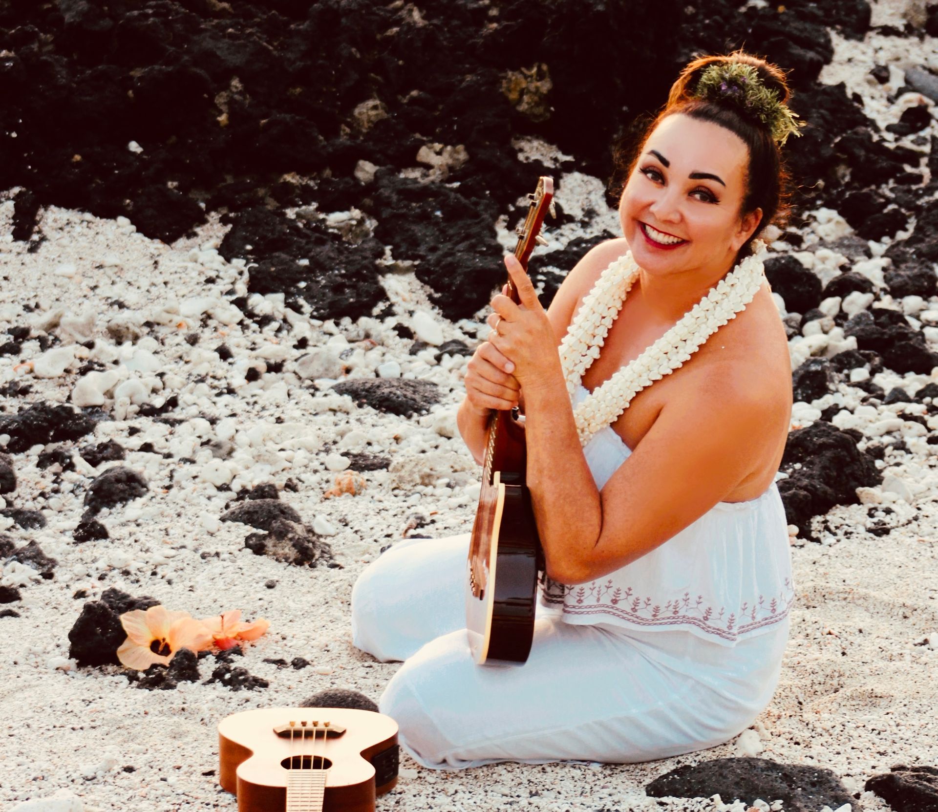 A woman in a white dress is holding a guitar on the beach
