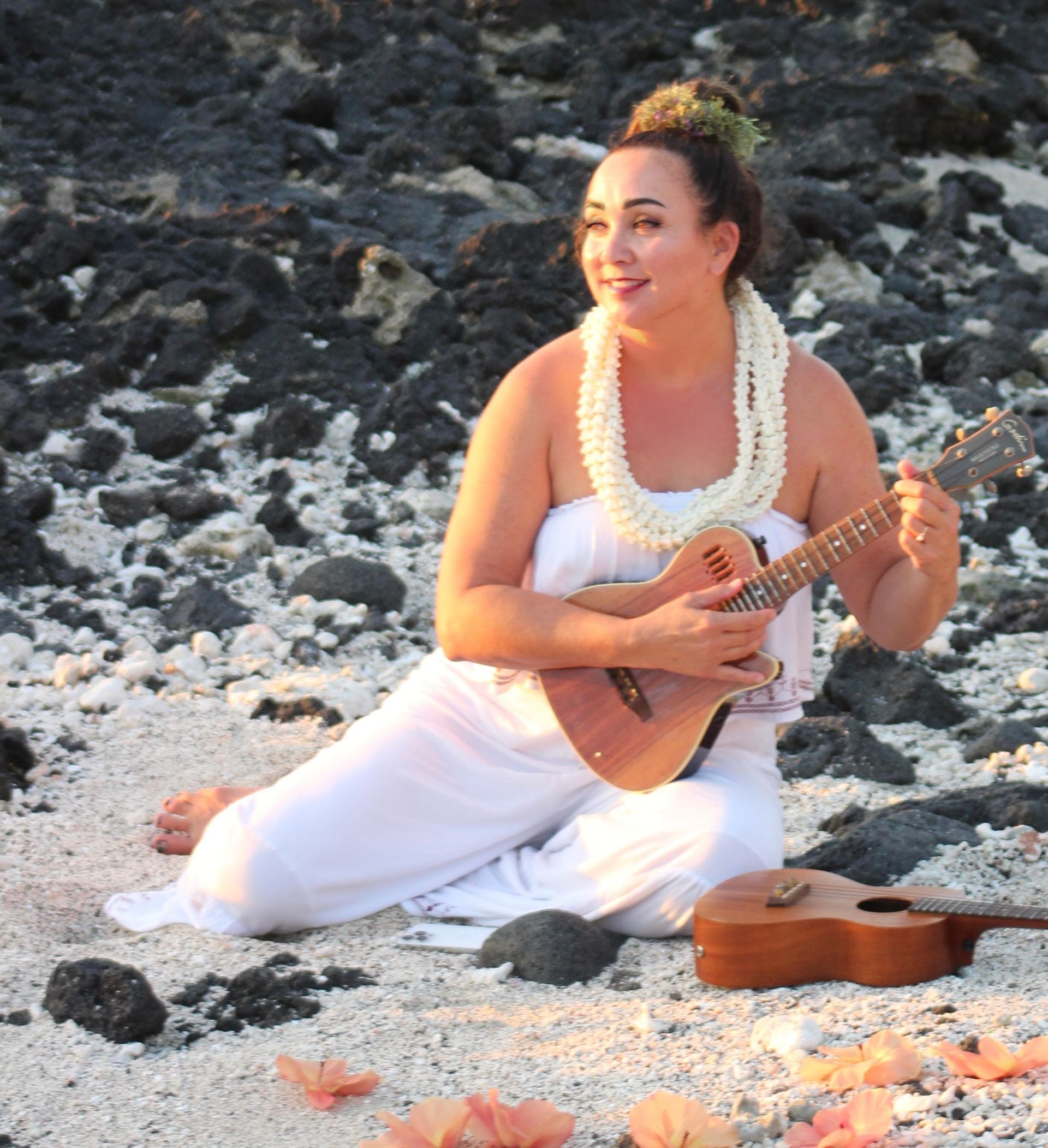 A woman in a white dress is playing a guitar on the beach