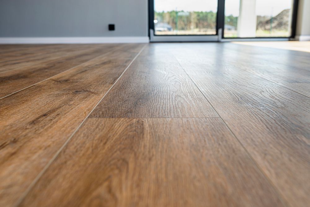 A low-angle view of warm, textured brown wood-look flooring stretching toward a window and gray wall in a modern room.