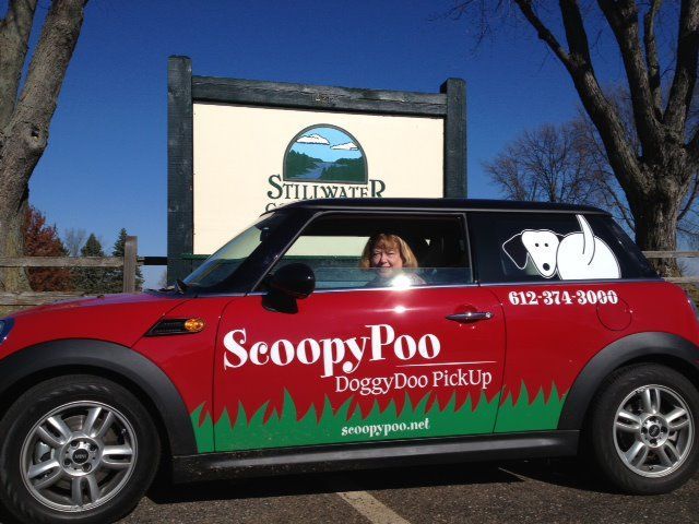 Red car with "ScoopyPoo Doggy Doo Pickup" logo; woman inside, Stillwater, MN sign in background.