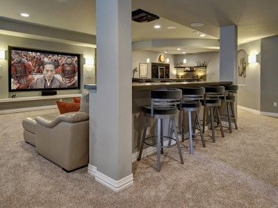 A basement with a bar , stools , a couch and a flat screen tv.