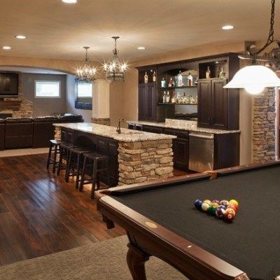 A pool table in a basement with a kitchen in the background