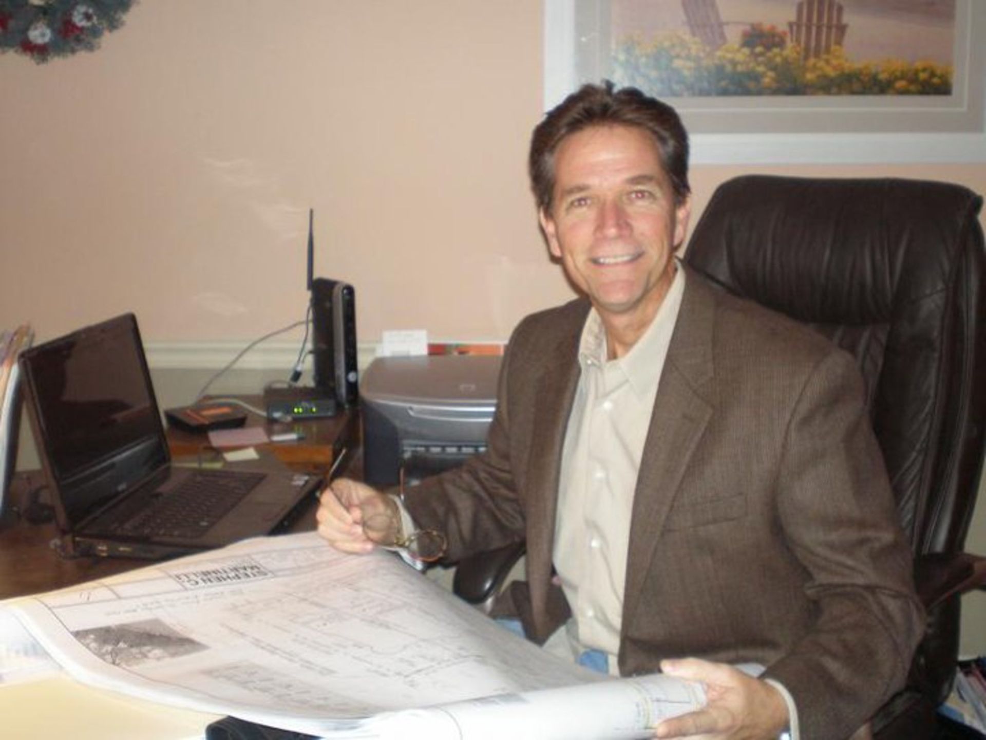 A man in a suit is sitting at a desk looking at a blueprint