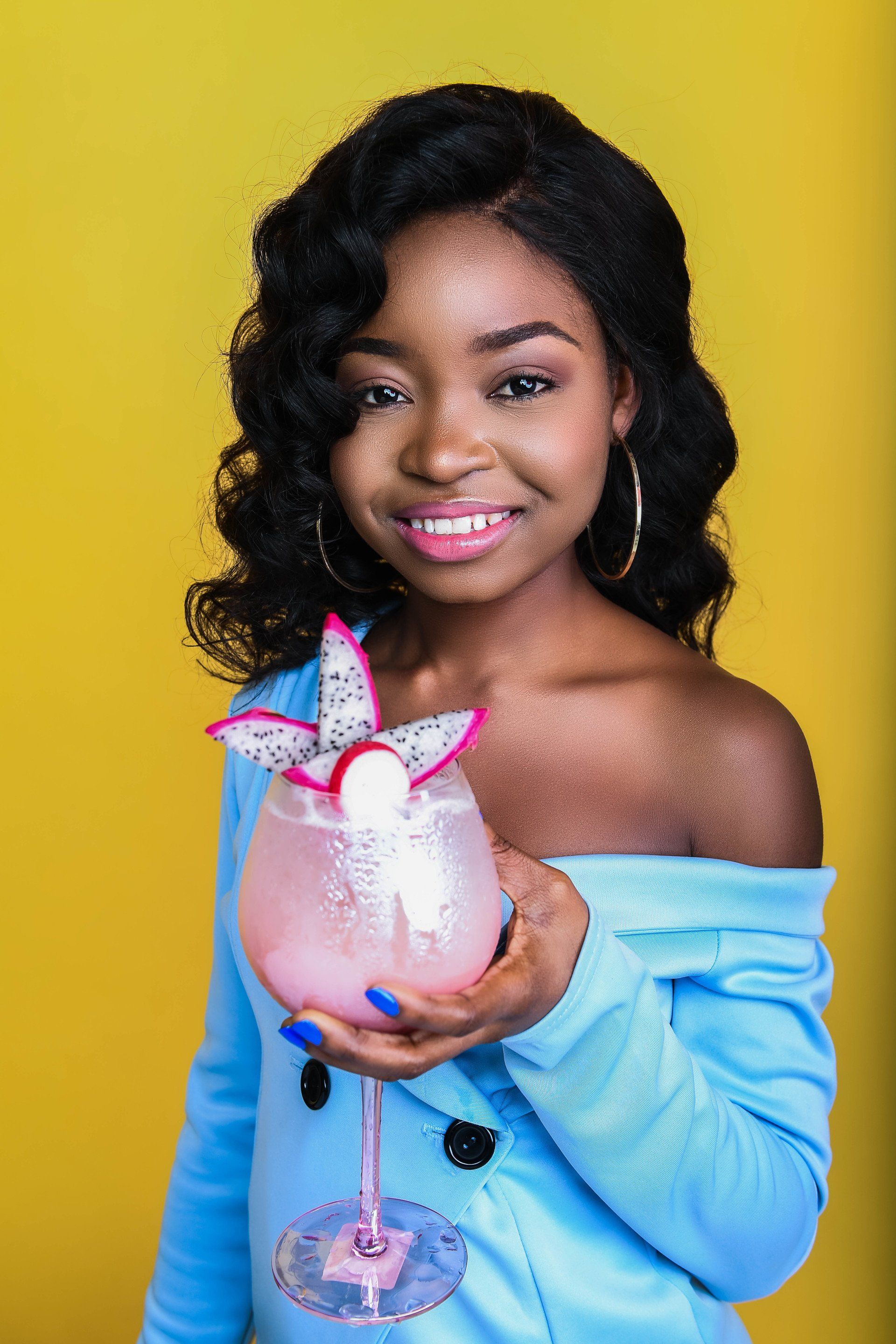 A woman is holding a glass of pink liquid with a dragon fruit on it.