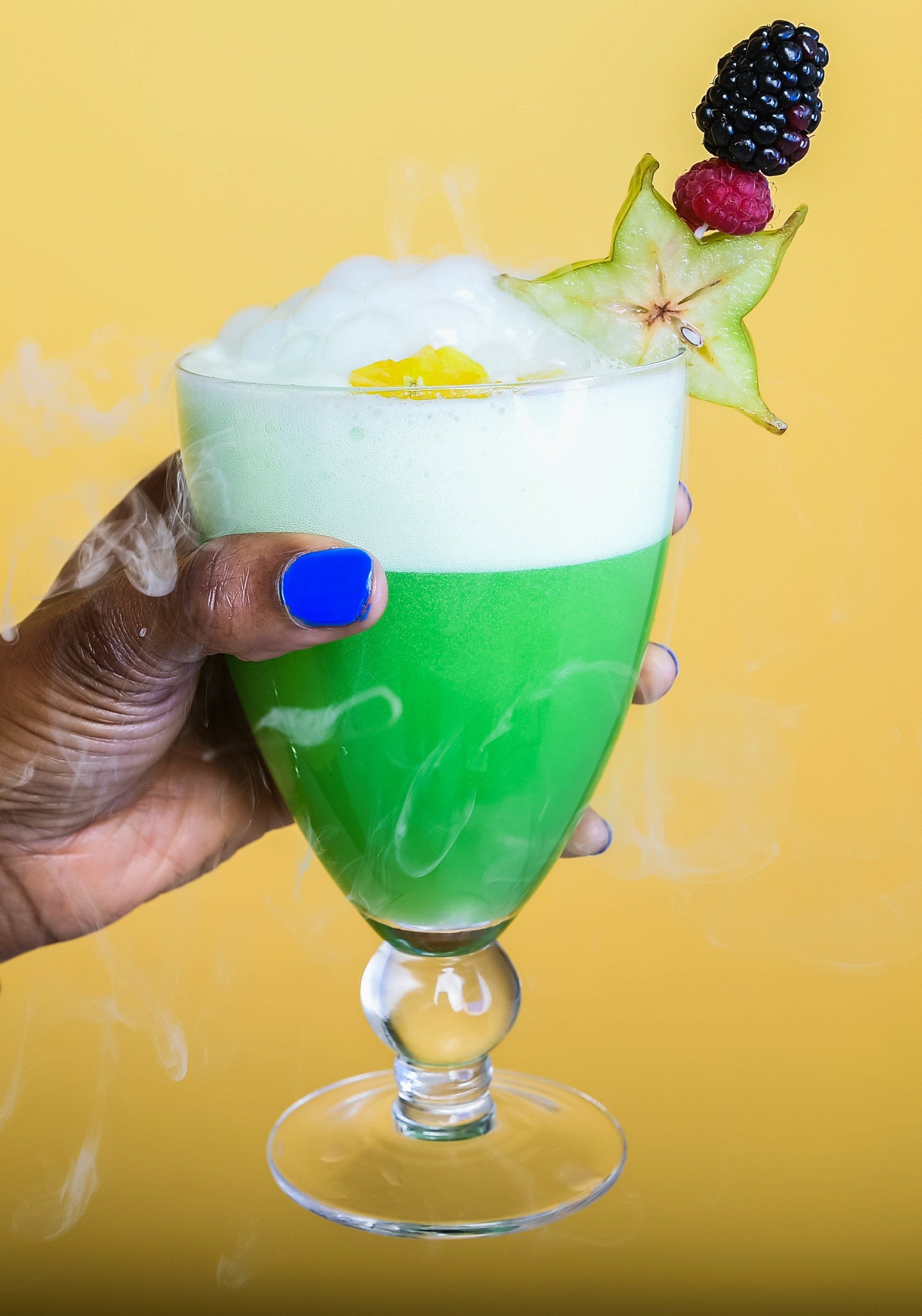 A person is holding a green cocktail with a star fruit on top.