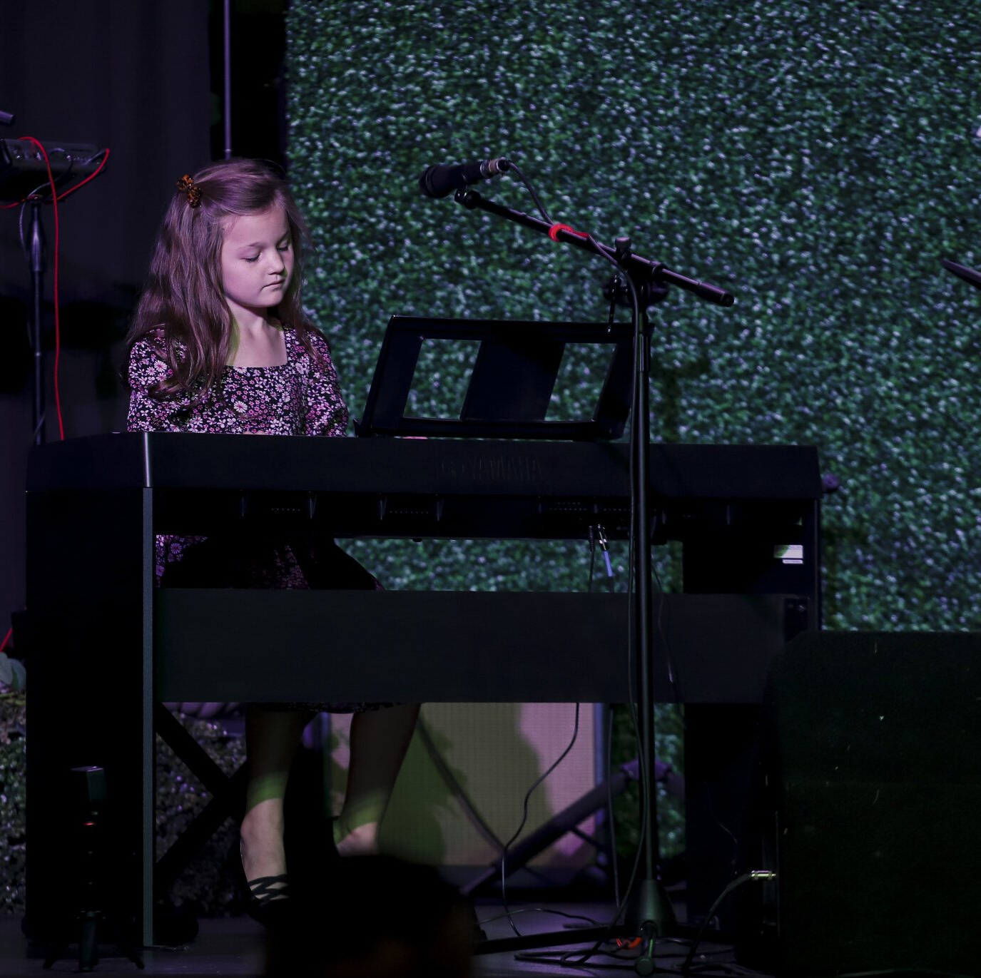 A little girl is playing a keyboard on a stage in front of a microphone.