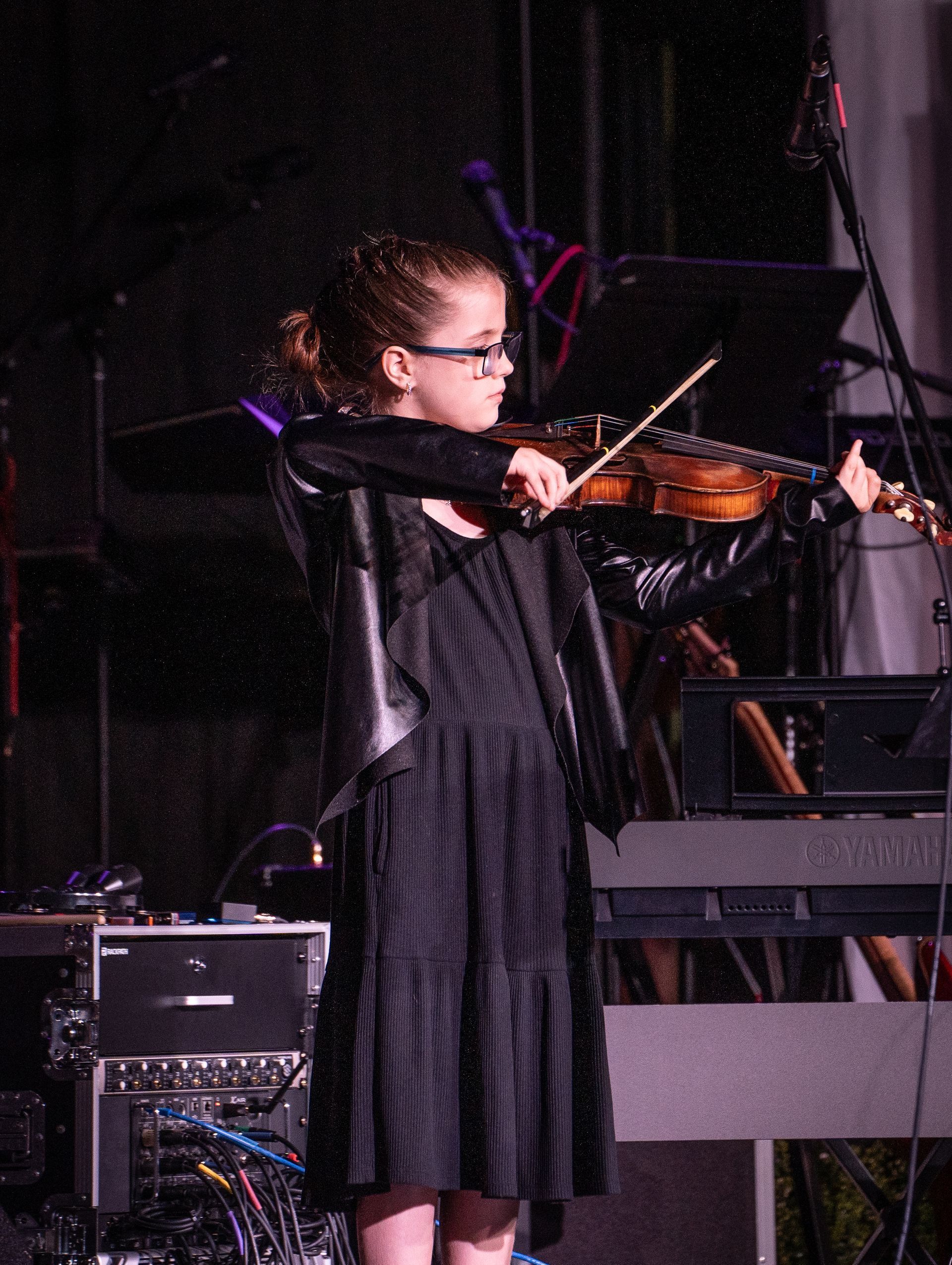 A young girl in a black dress is playing a violin on stage