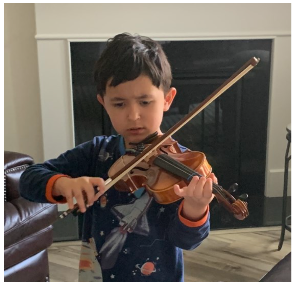 A young boy is playing a violin in front of a fireplace