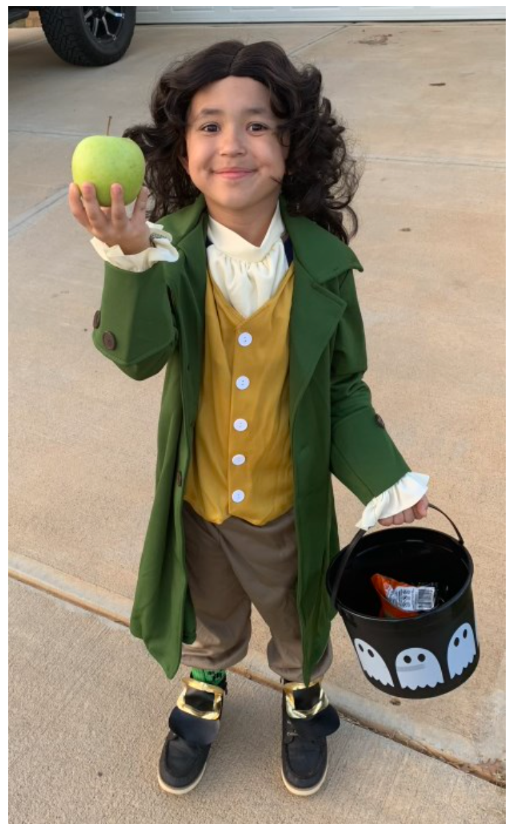 A young boy in a costume is holding an apple and a trick or treat bucket